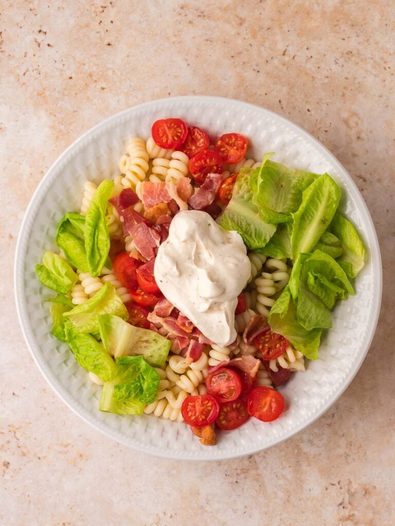 BLT pasta salad ingredients added to a large white bowl before mixing.