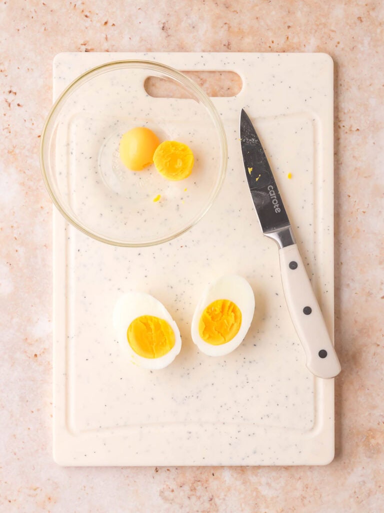 Hard boiled eggs sliced in half with yolks removed into a bowl.
