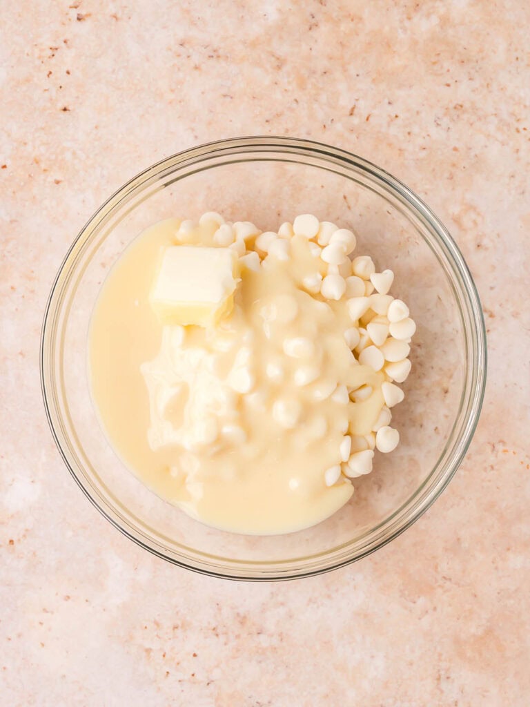 White chocolate chips, sweetened condensed milk, and butter in a glass bowl ready to be melted for layered fudge.