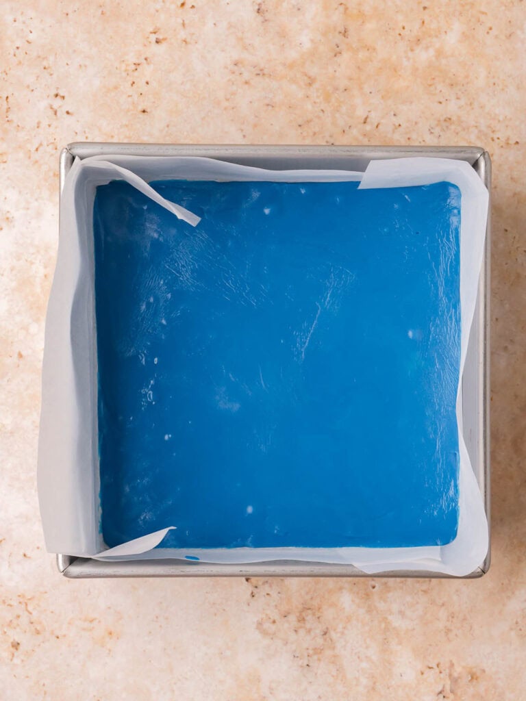 Blue fudge layer spread into a parchment-lined square baking dish.