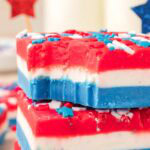 Close-up side view of layered patriotic fudge showing the creamy red, white, and blue layers with star sprinkles.