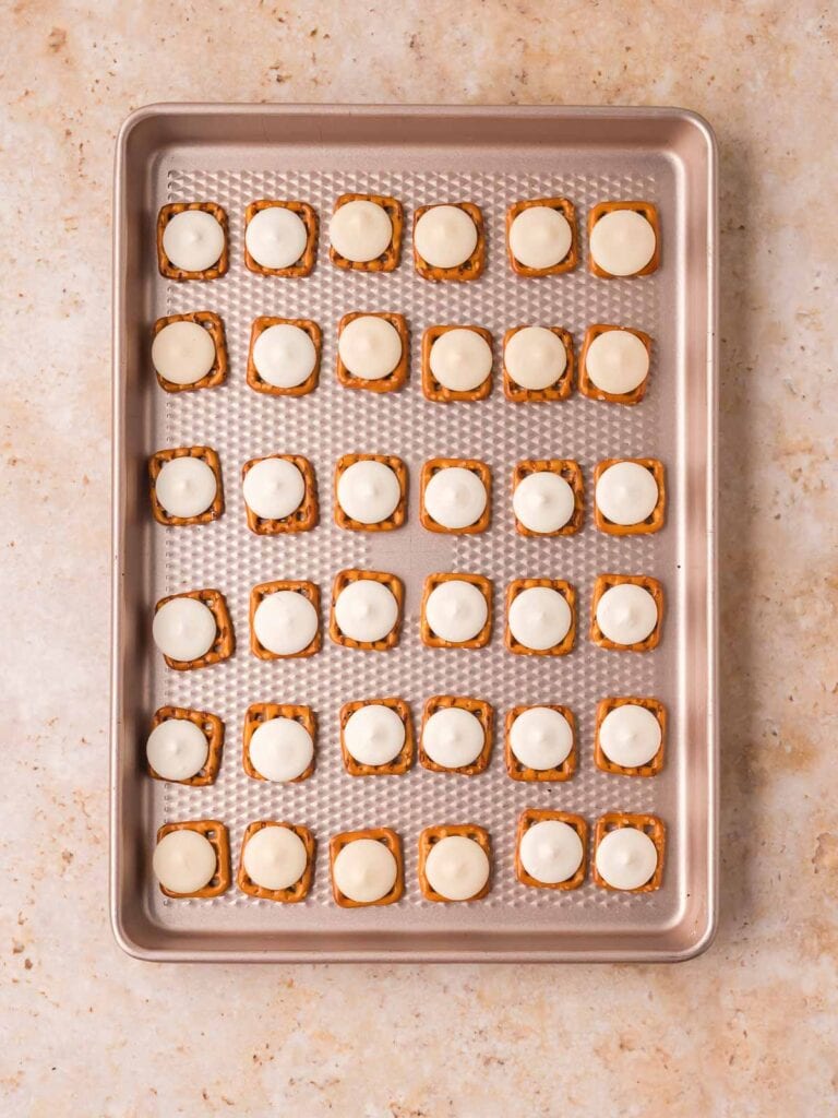 Pretzels topped with white candy melts arranged on a baking sheet before baking.