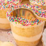 Gold spoon dipping into a finished dot cake topped with rainbow nonpareils showing the vanilla cake and buttercream layers inside by Tessie's Table.