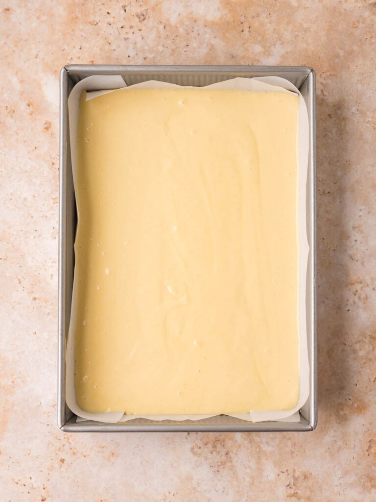Vanilla cake batter spread evenly in a parchment-lined 9x13 baking pan for dot cakes by Tessie's Table.