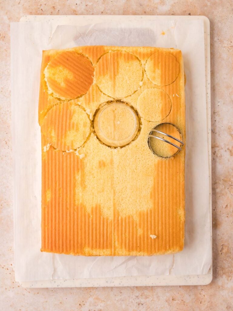 Cooled vanilla cake with round circles cut out using a dessert cup and small round cutter for dot cakes assembly by Tessie's Table.