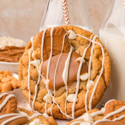 Biscoff stuffed white chocolate cookie leaning against a glass milk bottle showing the gooey Biscoff center, by Tessie's Table.
