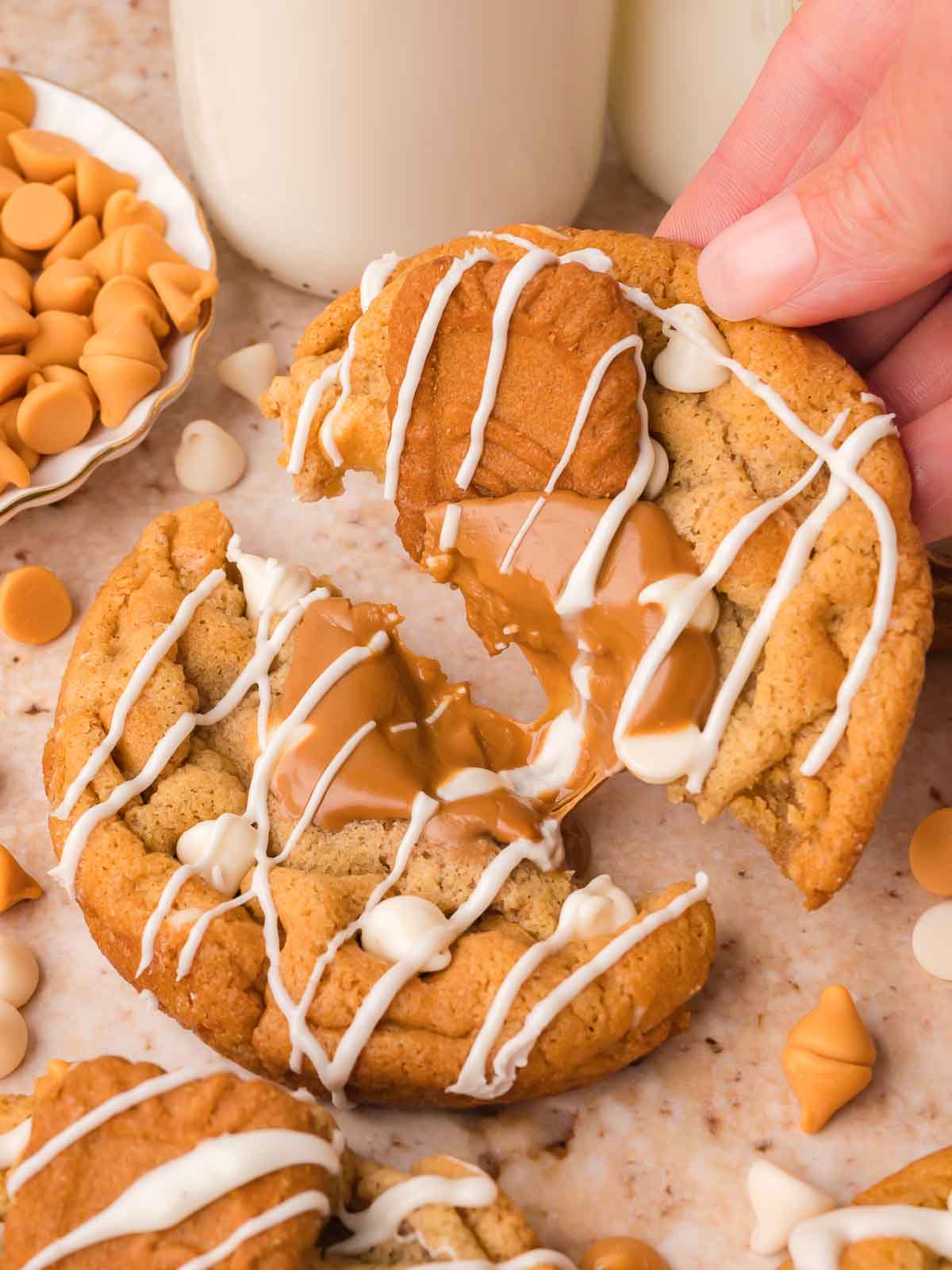 Hand breaking apart a Biscoff stuffed white chocolate cookie to reveal the gooey melted Biscoff center, with a glass of milk in the background.