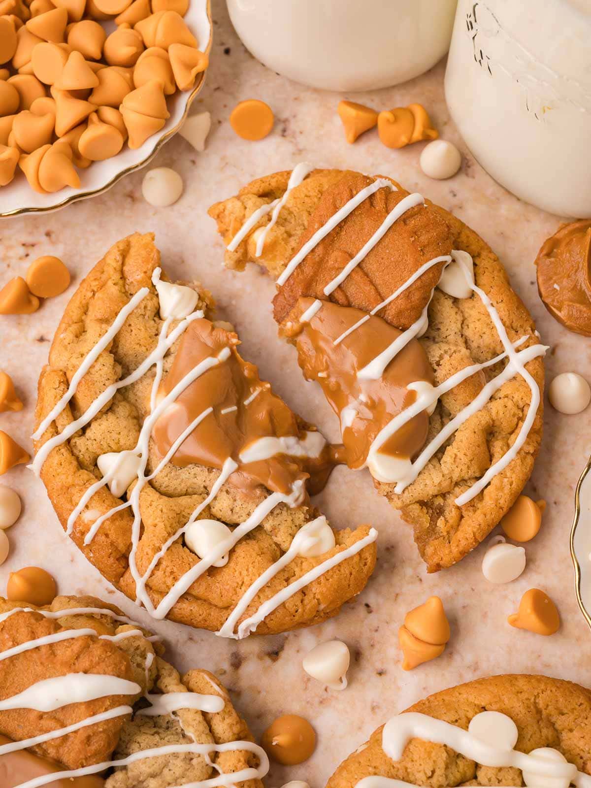 Two halves of a broken Biscoff stuffed white chocolate cookie showing the gooey Biscoff center, surrounded by scattered caramel and white chocolate chips, by Tessie's Table.