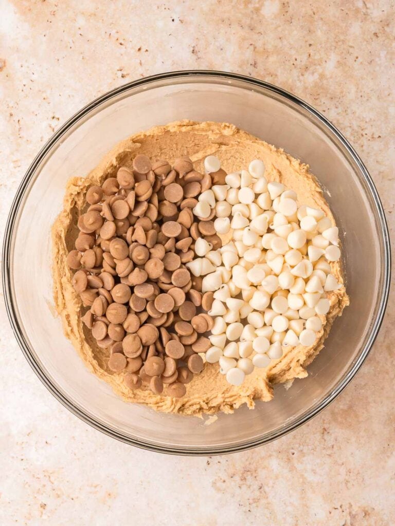 Cookie dough in a glass bowl with Biscoff chips and white chocolate chips on top before folding in, for Biscoff Stuffed White Chocolate Cookies by Tessie's Table.
