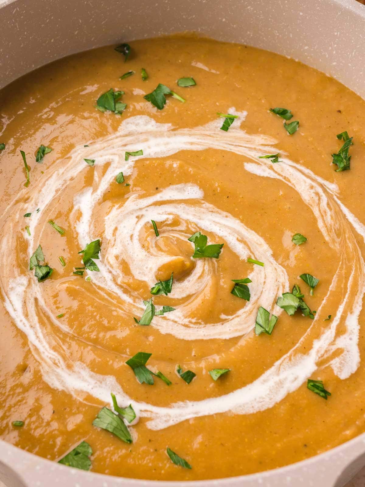 Overhead close-up of creamy homemade vegetable soup in a pot with a swirl of cream and chopped parsley by Tessie's Table.
