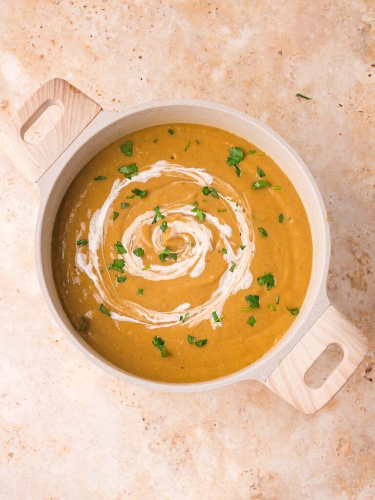Creamy blended homemade vegetable soup in a pot topped with a swirl of cream and fresh parsley by Tessie's Table.