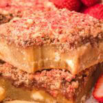 Two strawberry crunch blondies stacked with a bite taken from the top bar.