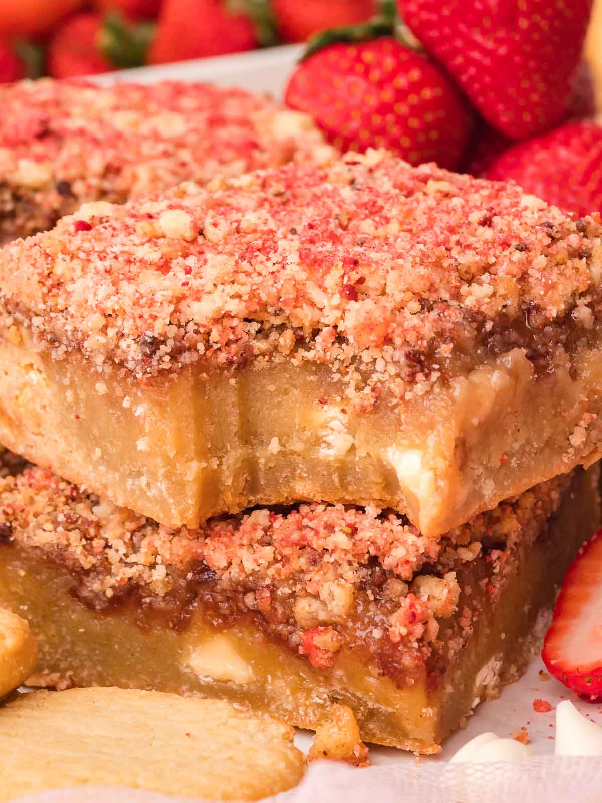 Two strawberry crunch blondies stacked with a bite taken from the top bar.