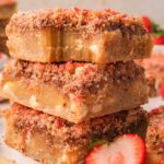 A stack of three strawberry crunch blondies topped with strawberry shortcake crumble, with fresh strawberries alongside.