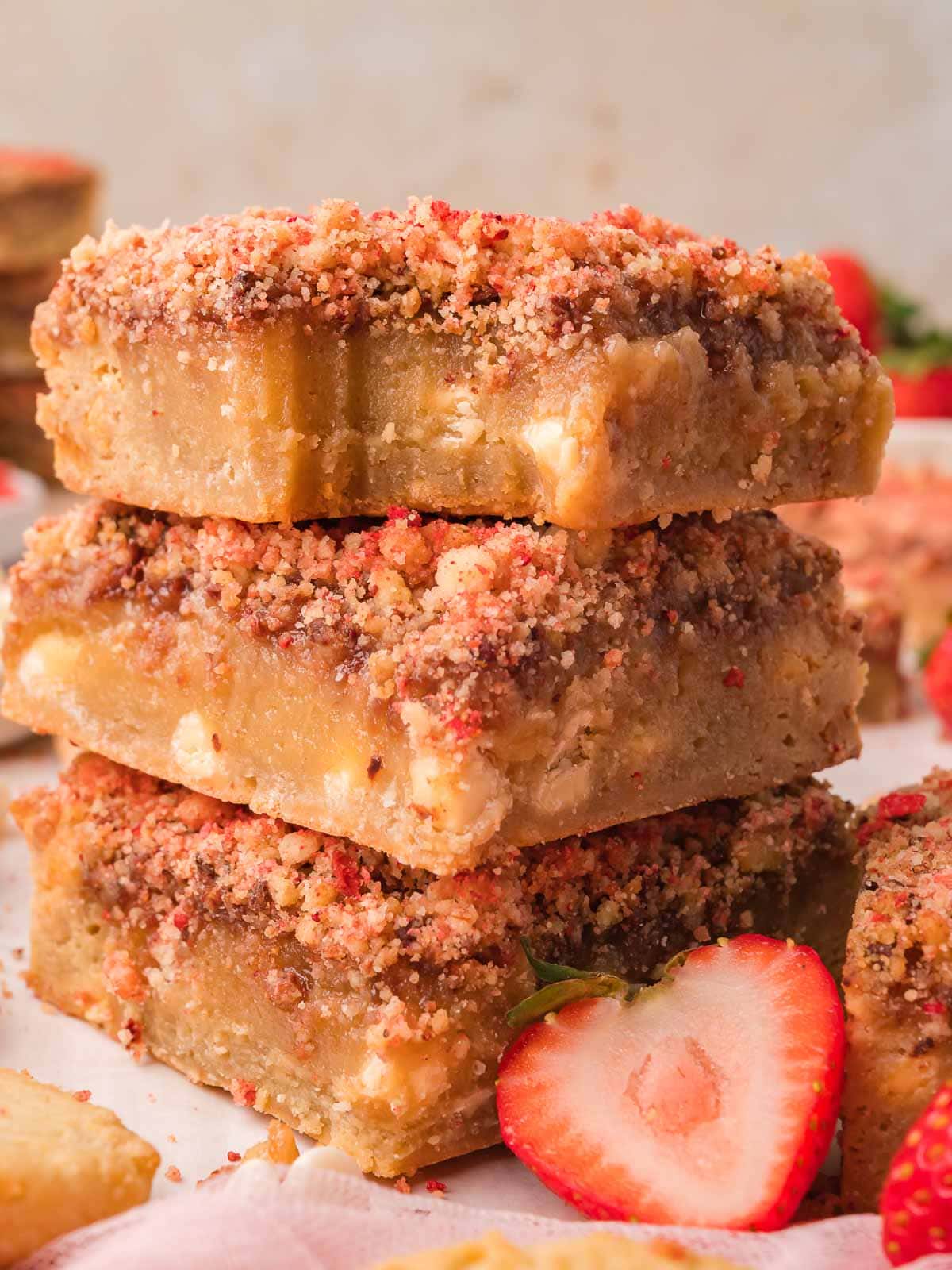 A stack of three strawberry crunch blondies topped with strawberry shortcake crumble, with fresh strawberries alongside.