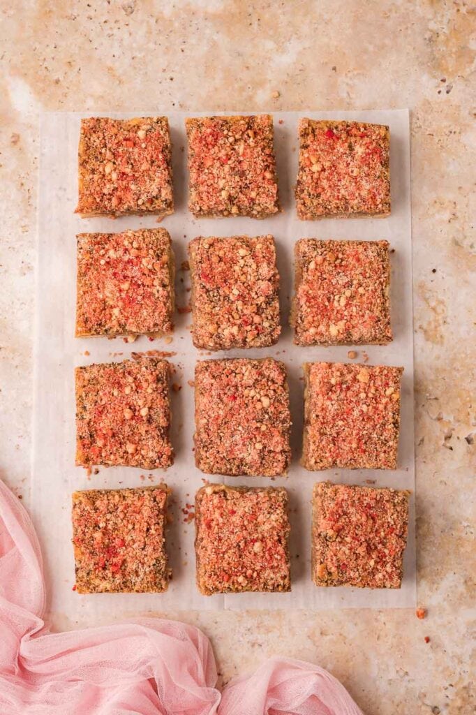Alt textBaked strawberry crunch blondies cut into twelve squares on parchment paper.