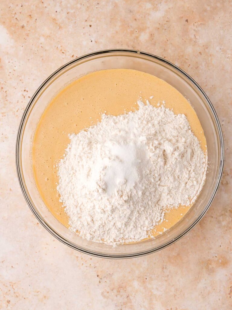 Flour and salt added to the wet blondie batter in a glass mixing bowl.