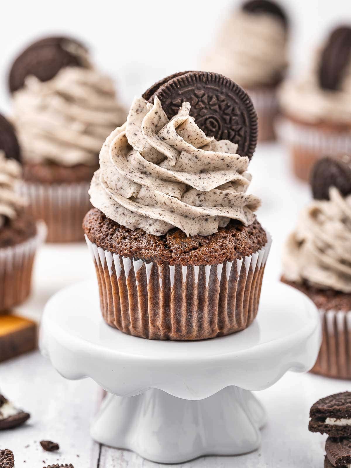 Oreo cupcake with cookies and cream frosting on a white cake stand.