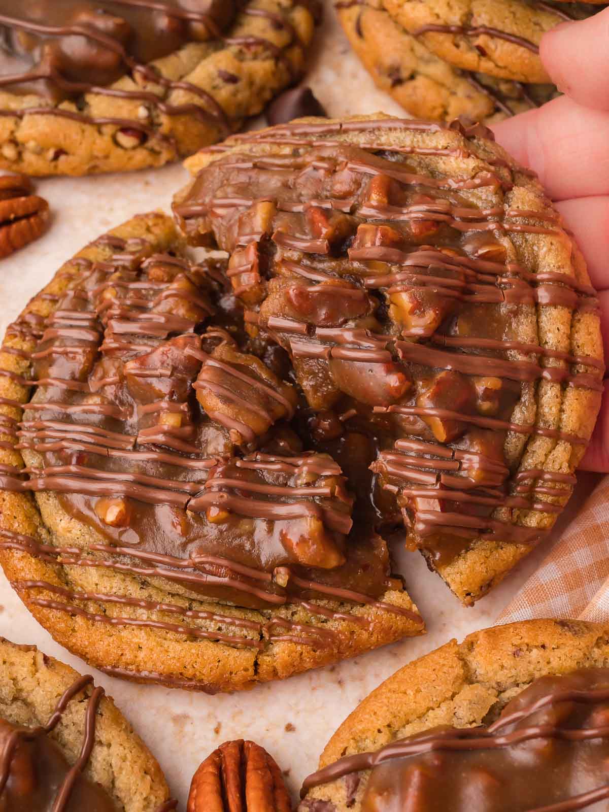 Hand holding a large pecan pie cookie topped with pecan filling and chocolate drizzle by Tessie's Table.