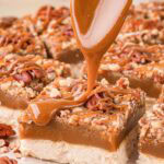 Caramel being spooned over a salted caramel pecan bar showing the thick caramel layer by Tessie's Table.