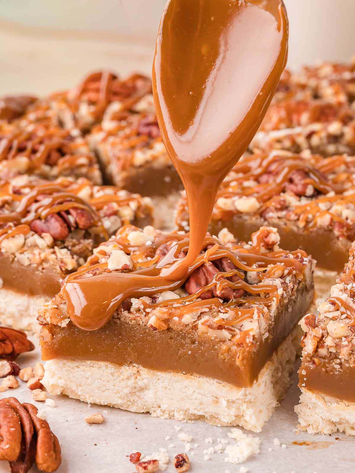 Caramel being spooned over a salted caramel pecan bar showing the thick caramel layer by Tessie's Table.
