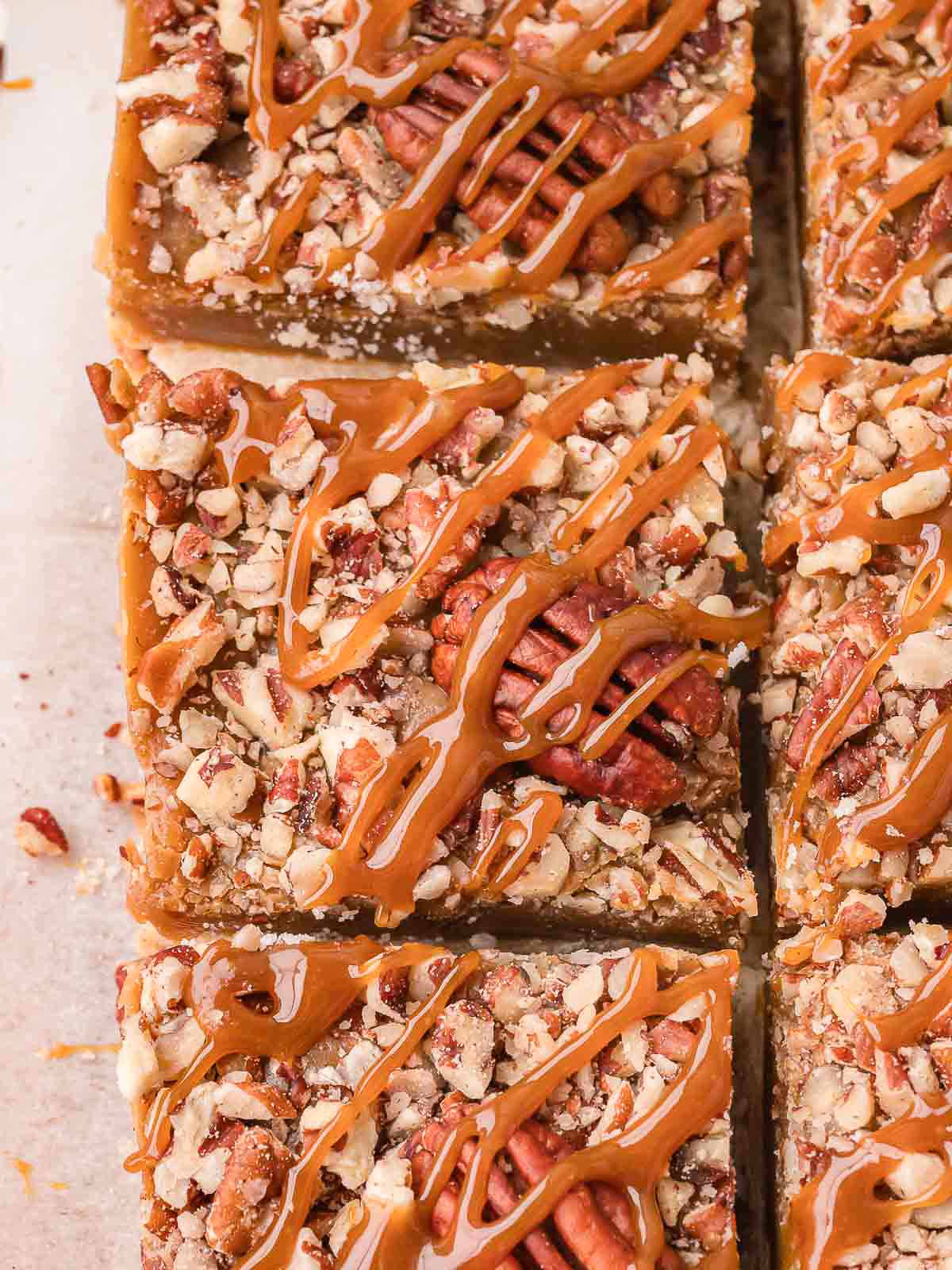 Salted caramel pecan bars cut into squares with pecan halves and caramel drizzle on parchment by Tessie's Table.