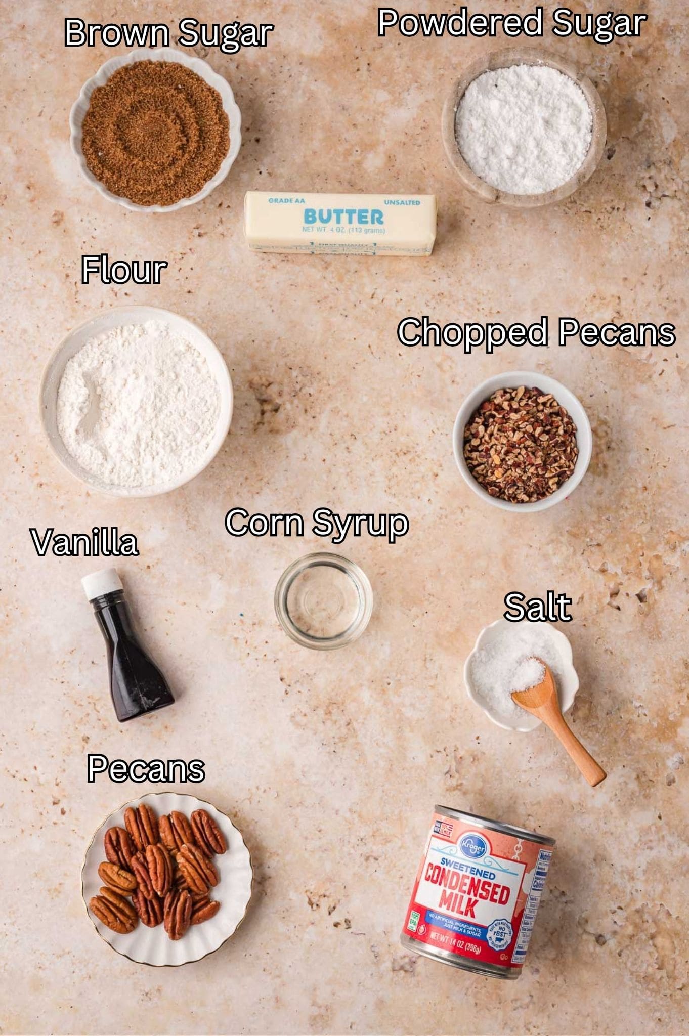 Ingredients for salted caramel pecan bars including butter, brown sugar, condensed milk, flour and pecans labeled on a counter by Tessie's Table.