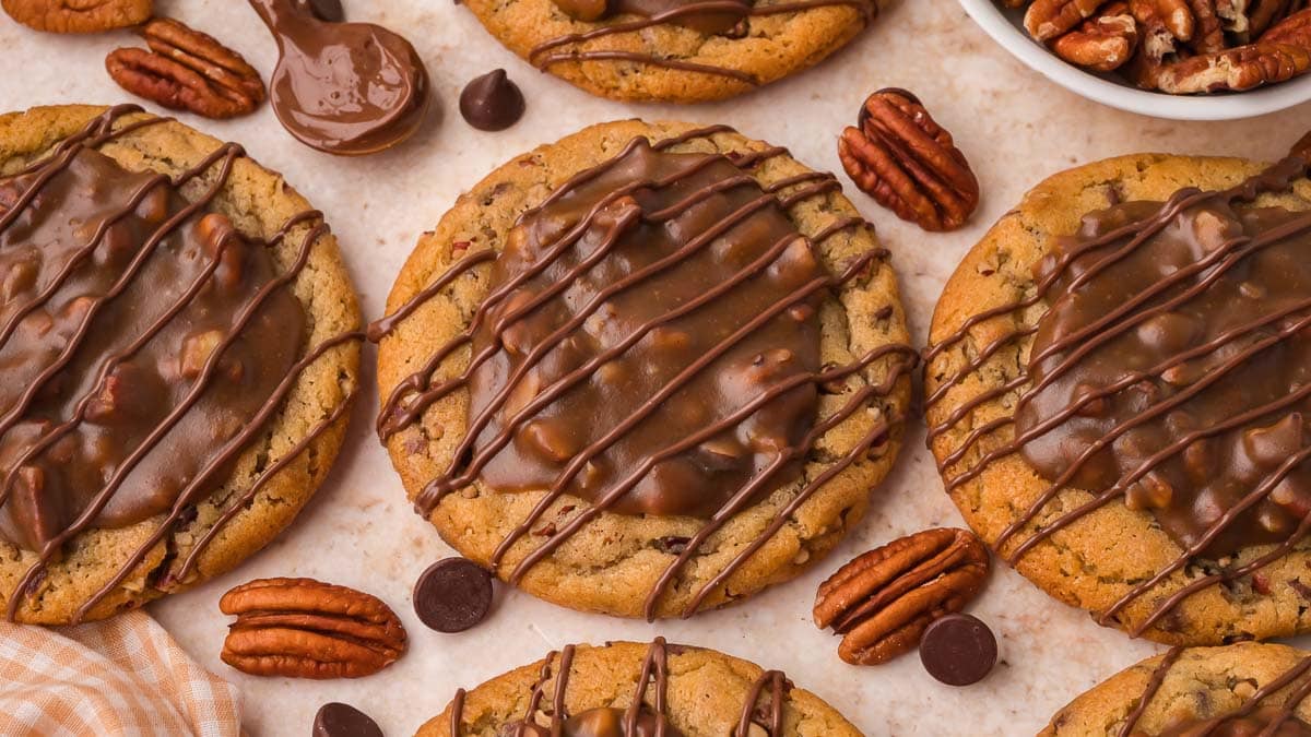 Three pecan pie cookies with chocolate drizzle and whole pecans on parchment paper by Tessie's Table.
