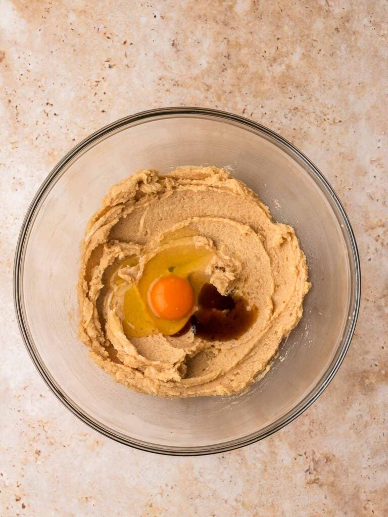 Egg and vanilla added to creamed butter and sugar in a glass bowl for pecan pie cookies by Tessie's Table.