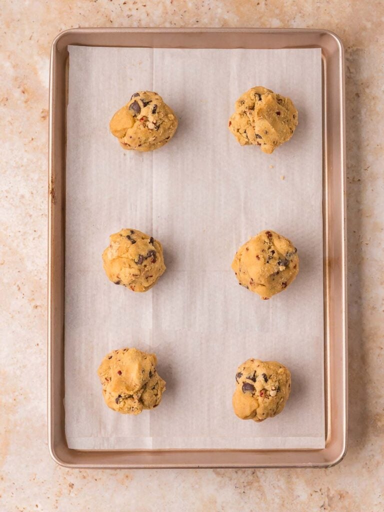 Six pecan pie cookie dough balls on a parchment lined baking sheet by Tessie's Table.