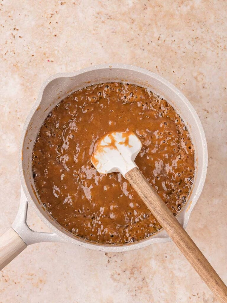 Salted caramel bubbling in a saucepan with a spatula for salted caramel pecan bars by Tessie's Table.