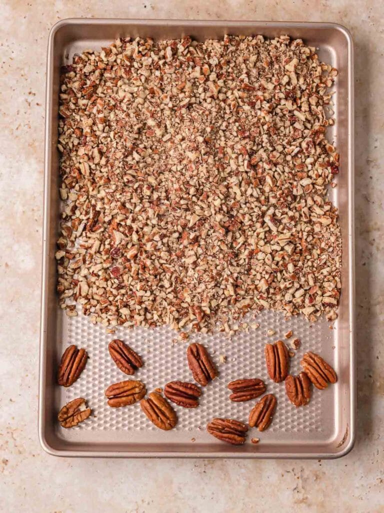Chopped pecans and pecan halves toasting on a sheet pan for salted caramel pecan bars by Tessie's Table.