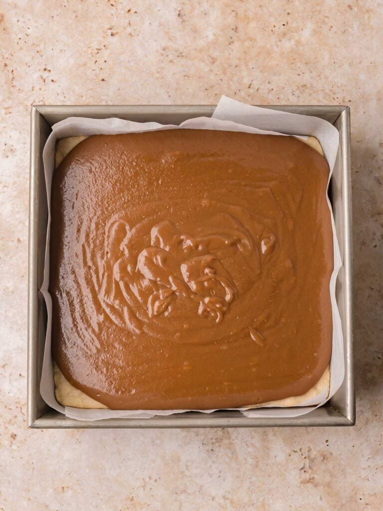 Thick salted caramel poured over a baked shortbread base in a square pan by Tessie's Table.