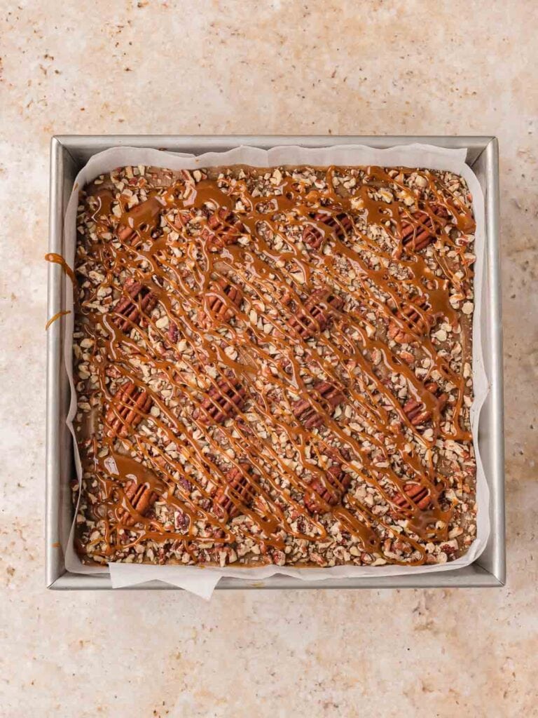 Toasted pecans and caramel drizzle over the caramel layer in the pan for salted caramel pecan bars by Tessie's Table.