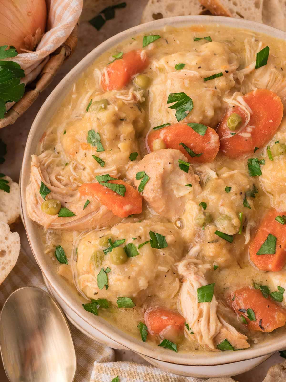 A bowl of slow cooker chicken and dumplings topped with fresh parsley and served with bread by Tessie's Table.