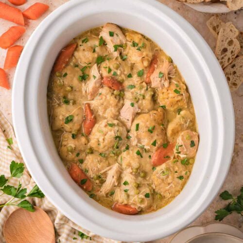 Overhead view of slow cooker chicken and dumplings with carrots and bread on the side by Tessie's Table.