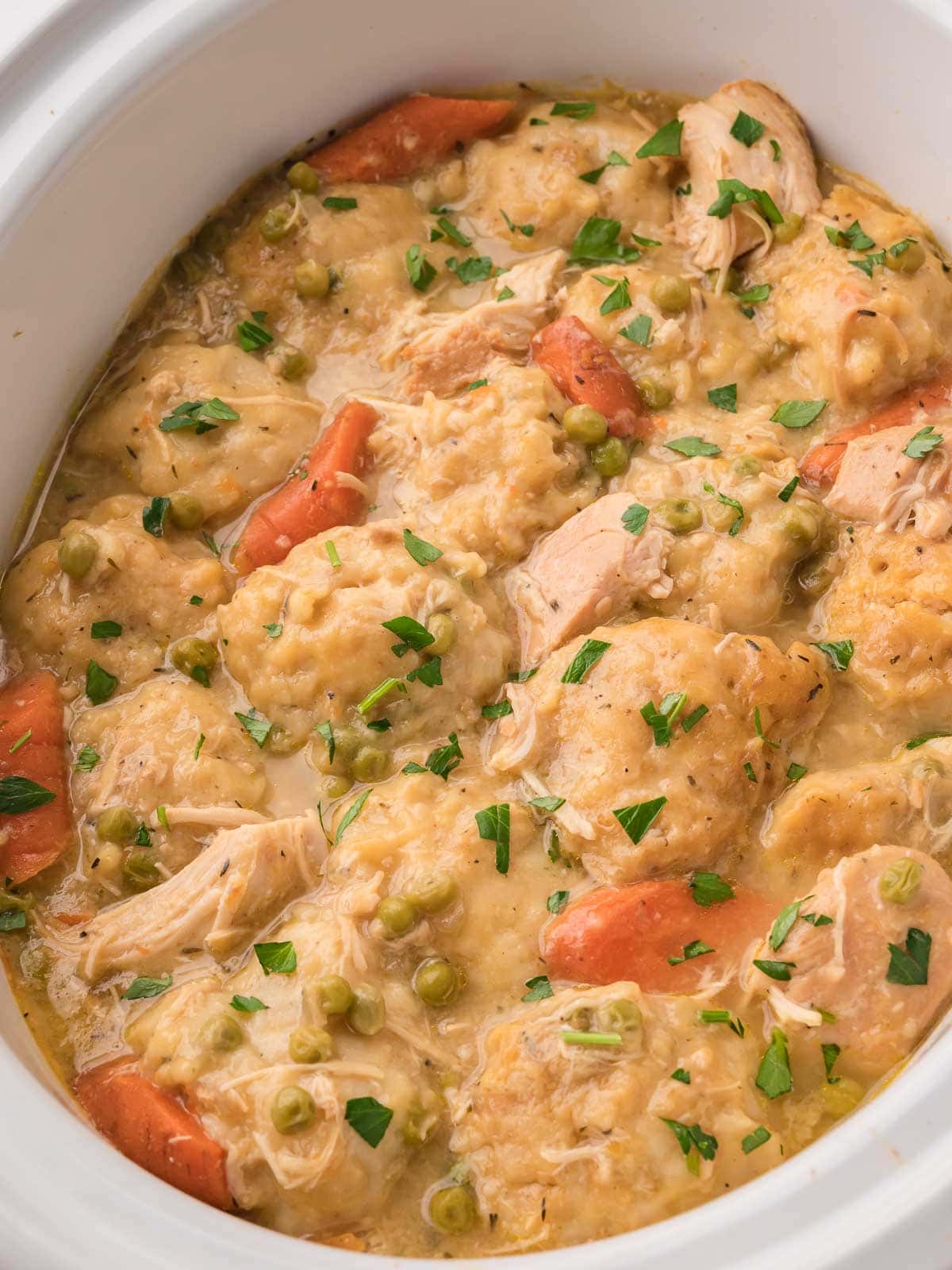 Creamy slow cooker chicken and dumplings with shredded chicken, carrots, and peas by Tessie's Table.