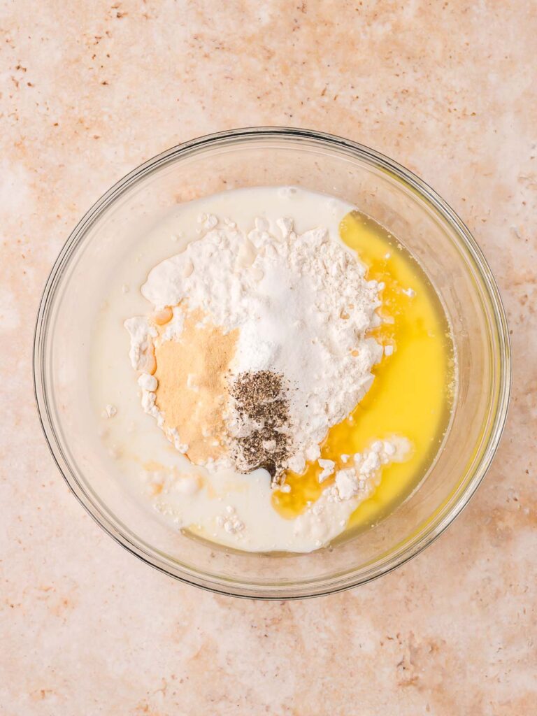 Flour, milk, melted butter, and seasonings in a glass bowl for homemade dumplings by Tessie's Table.