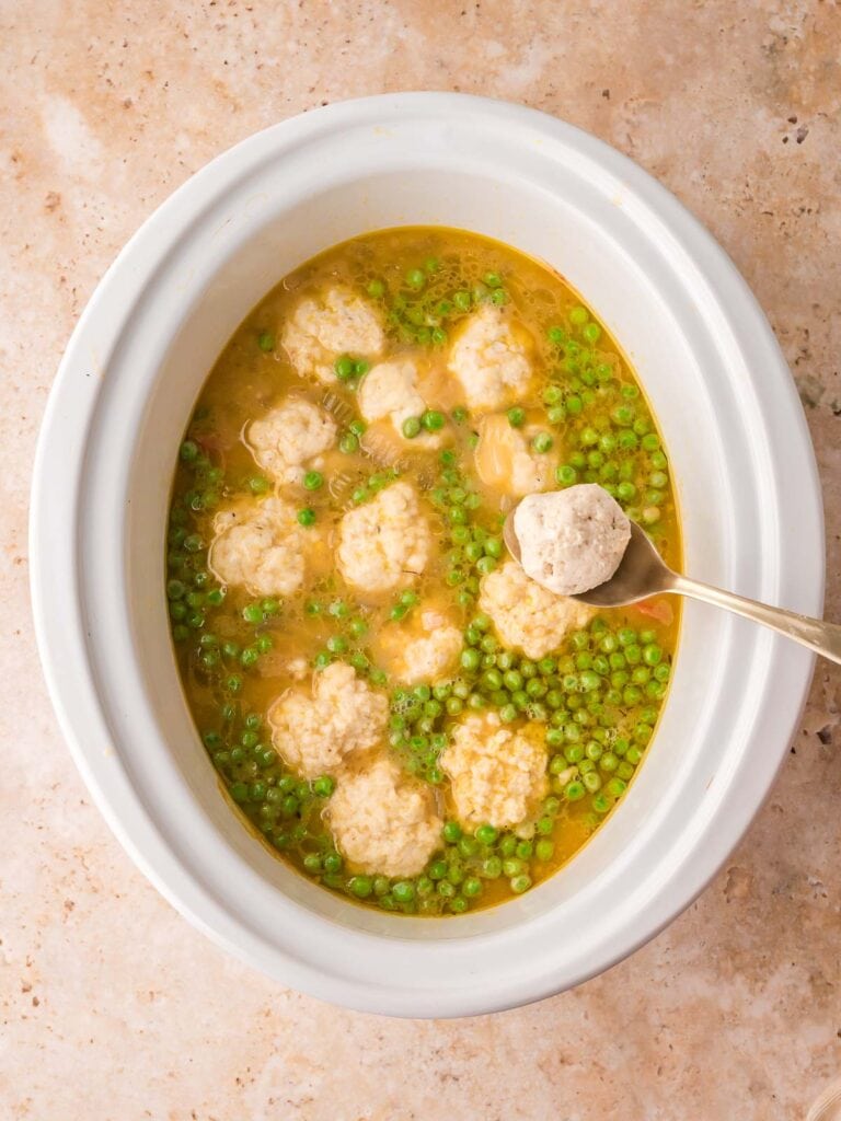 Spoonfuls of dumpling dough dropped over the chicken mixture and peas in the slow cooker by Tessie's Table.