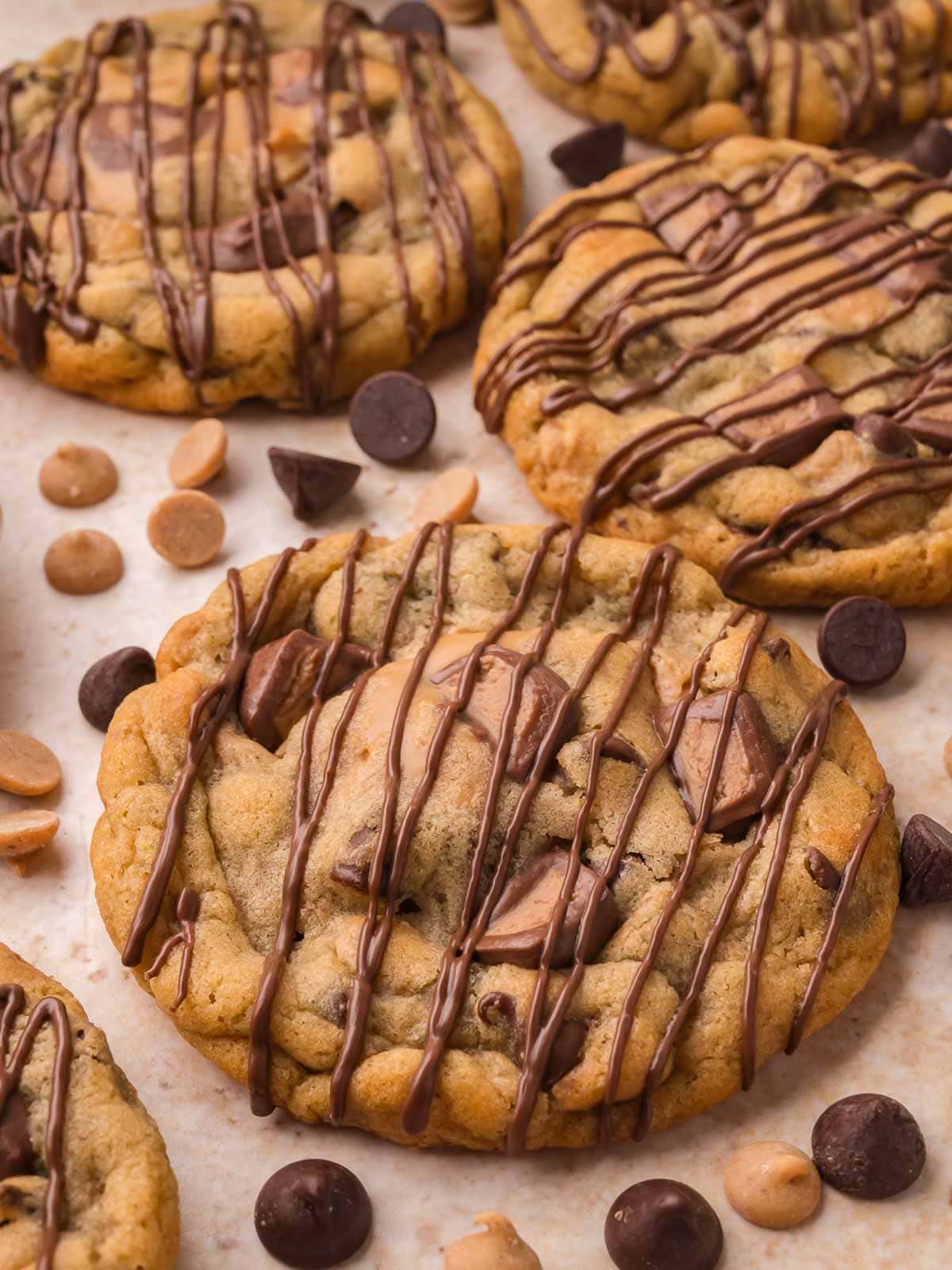 Close up of Nutella stuffed Reese's cookies with chocolate drizzle and peanut butter cup pieces on parchment by Tessie's Table.