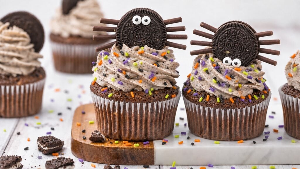 Spider Oreo cupcake for Halloween with chocolate stick legs, candy eyes, and orange and purple sprinkles.