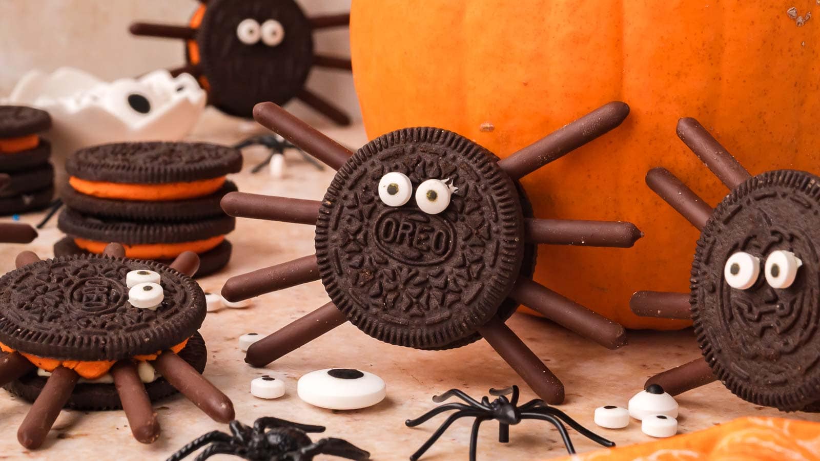 Oreo spider cookies with orange cream filling propped against a pumpkin by Tessie's Table.