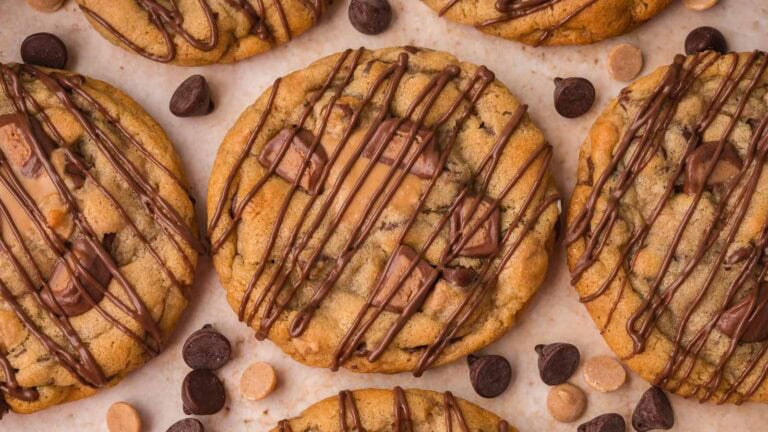 Overhead view of Nutella stuffed Reese's cookies with chocolate drizzle and peanut butter cup pieces on top by Tessie's Table.