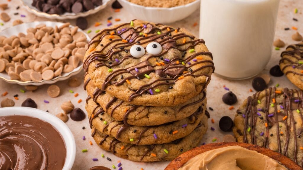 Stack of Halloween monster Nutella stuffed Reese's cookies with candy eyes, chocolate drizzle and orange, purple and green sprinkles by Tessie's Table.