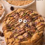 Halloween monster cookies with candy eyes, chocolate drizzle and orange, purple and green sprinkles, shown overhead and stacked beside a glass of milk by Tessie's Table.