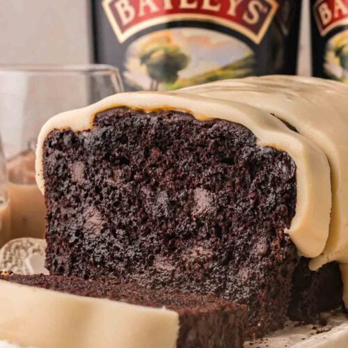 Close up of chocolate Baileys banana bread cut open to show melted chocolate chips in a dark crumb under white chocolate Baileys ganache by Tessie's Table.