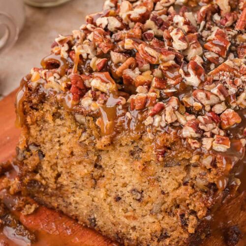 Caramel pecan banana bread cut open on a wooden board with a thick layer of caramel and chopped pecans on top by Tessie's Table.