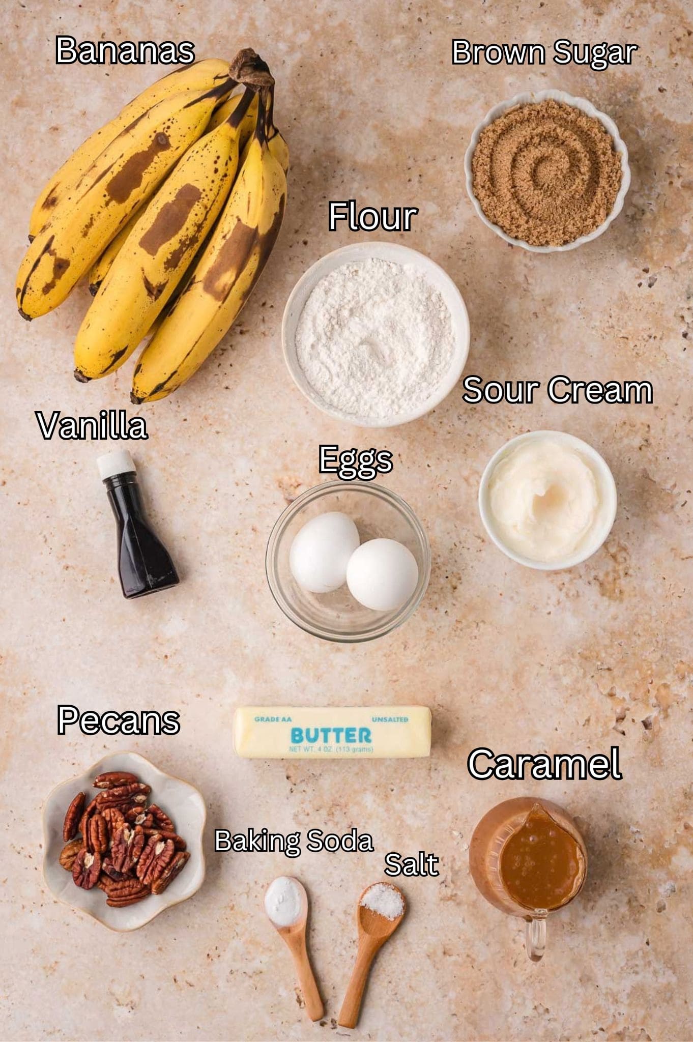 Labeled ingredients for caramel pecan banana bread including ripe bananas, brown sugar, flour, sour cream, eggs, vanilla, butter, pecans, caramel, baking soda and salt by Tessie's Table.