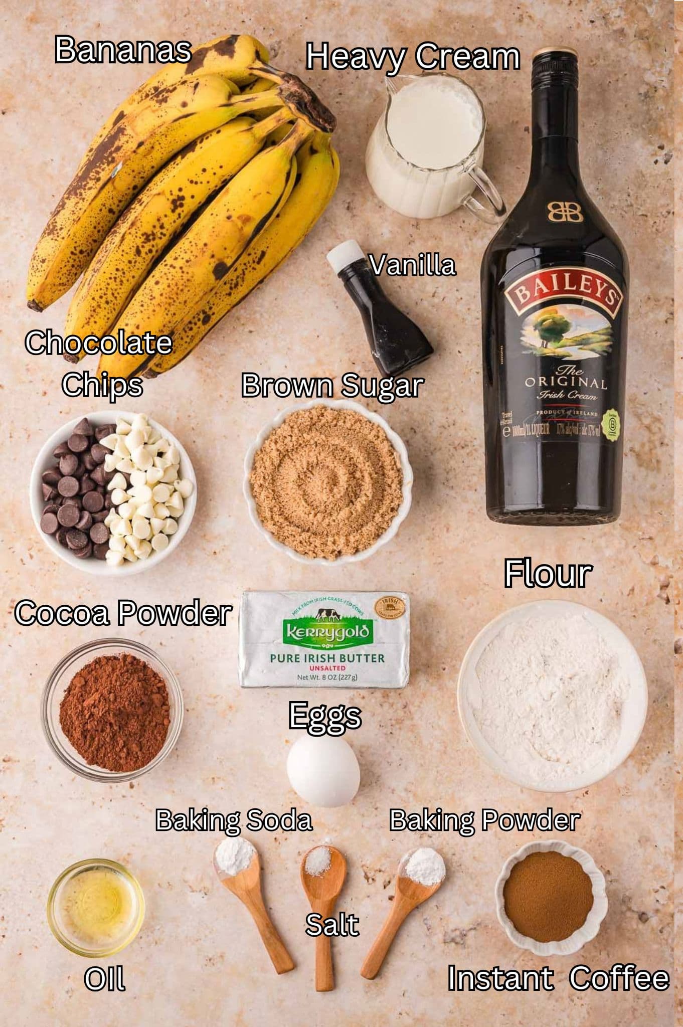 Labeled ingredients for chocolate Baileys banana bread including ripe bananas, heavy cream, vanilla, Baileys Irish Cream, dark and white chocolate chips, brown sugar, cocoa powder, butter, an egg, flour, oil, baking soda, baking powder, salt and instant coffee by Tessie's Table.
