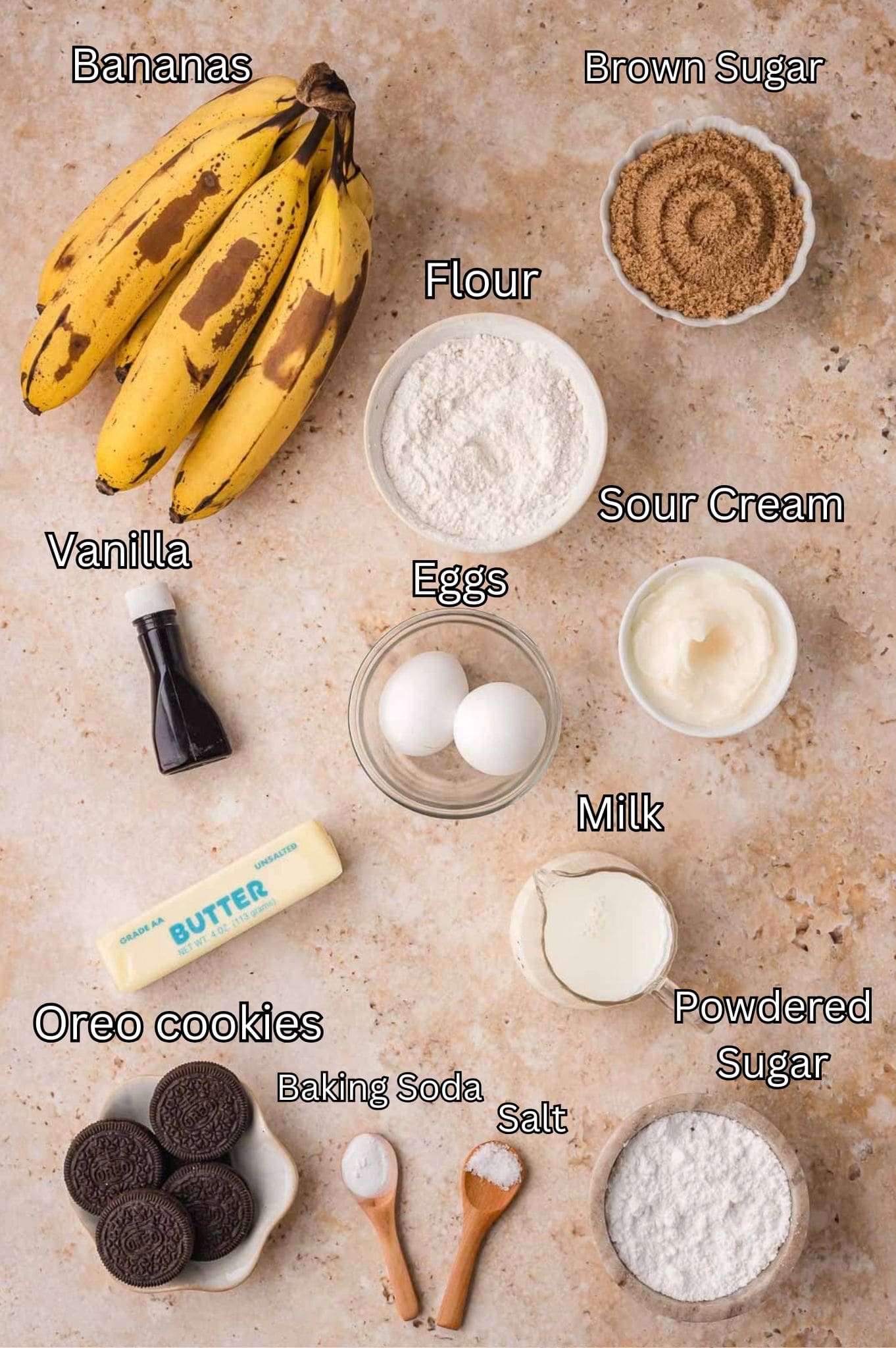 Labeled ingredients for Oreo banana bread including ripe bananas, brown sugar, flour, sour cream, eggs, vanilla, butter, milk, Oreo cookies, powdered sugar, baking soda and salt by Tessie's Table.